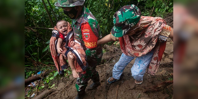 An Indonesian soldier helps a woman carry her baby as she makes her way through an area damaged by an earthquake-induced landslide near Mamuju, West Sulawesi, Indonesia, Saturday, January 16, 2021 (AP Photo / Yusuf Wahil)