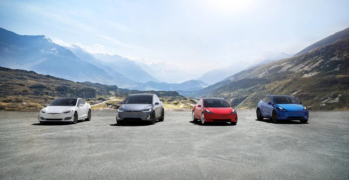 Four Tesla cars on a plot of gravel in the mountains.